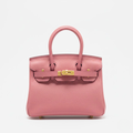 Pink handbag with gold hardware on a light gray background