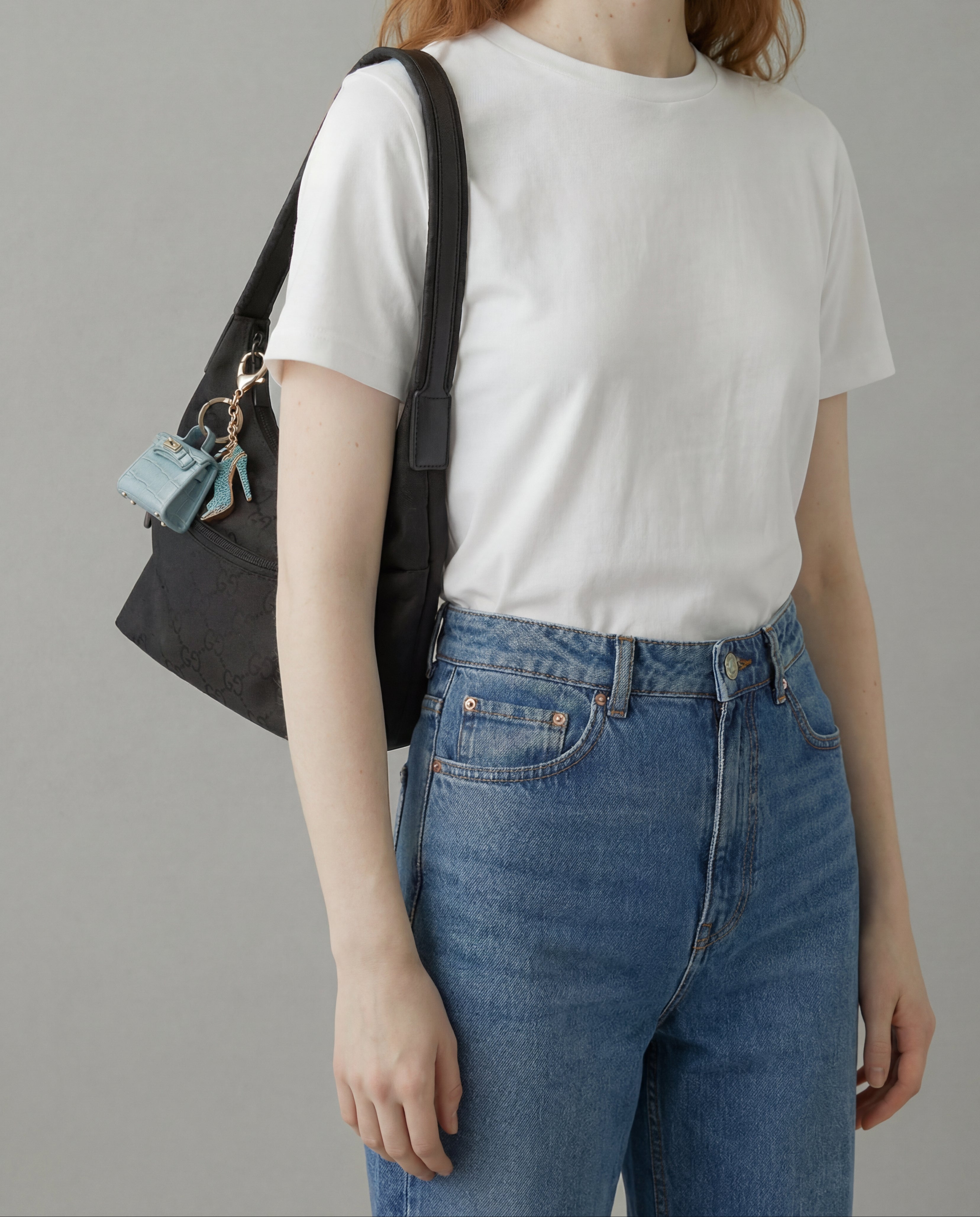 Person wearing a white t-shirt and blue jeans, holding a black bag against a gray background