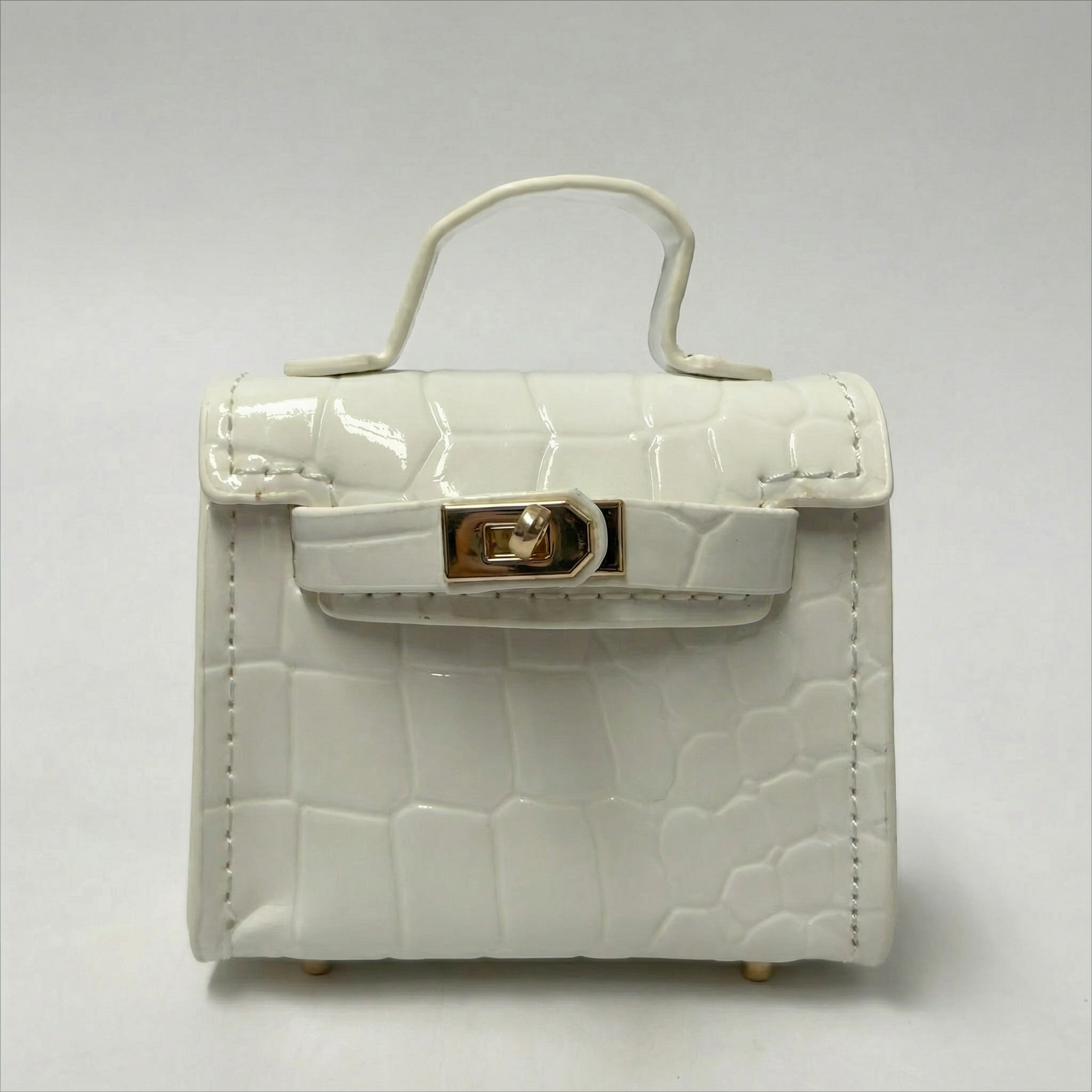 White crocodile-patterned handbag with a gold clasp on a light gray background